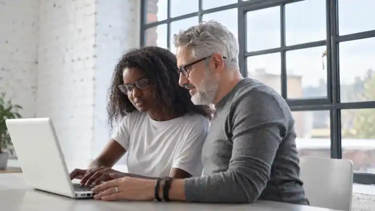 Dos colegas trabajando con una laptop en una mesa compartida