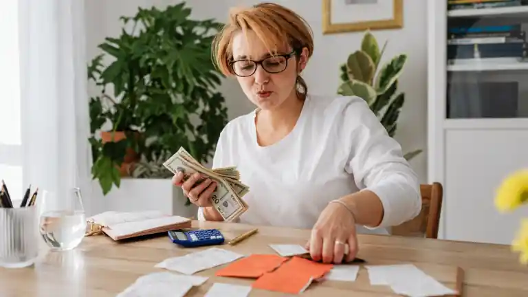 Una persona revisando efectivo y recibos junto a una calculadora y una libreta